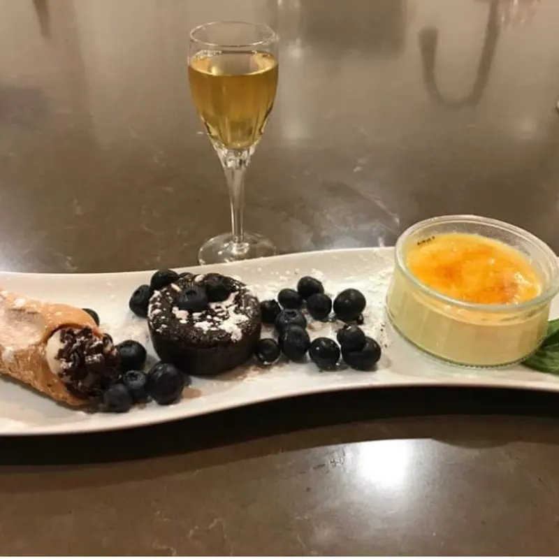 Dessert trio of cannoli, chocolate lava cake with blueberries, and crème brûlée served with wine