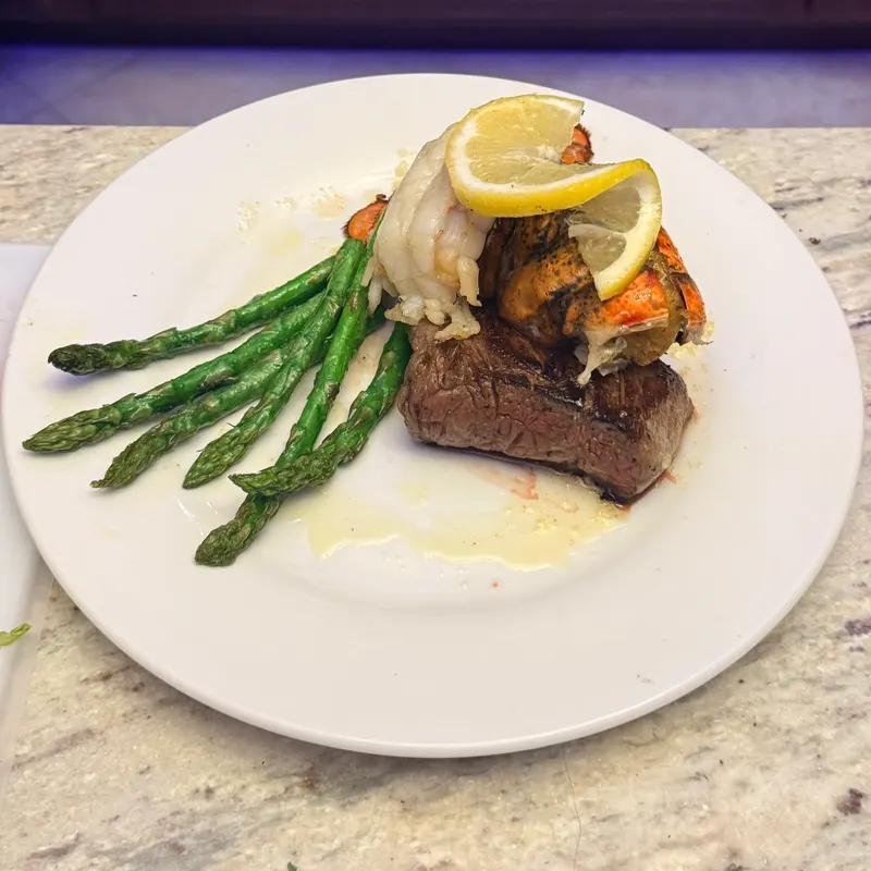 Surf and turf plate — grilled steak topped with a lobster tail, asparagus, and lemon